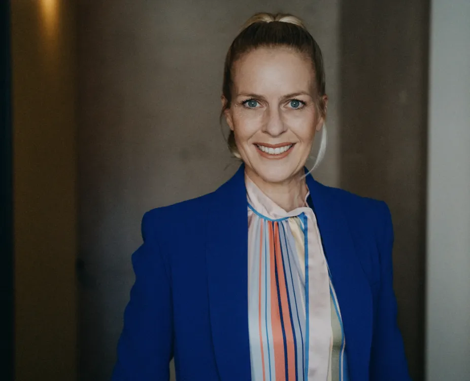 Alexandra von Lingen in gestreifter Bluse und blauem Blazer vor dunkelgrauer Wand - sie lächelt in die Kamera